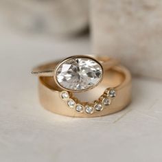 two gold wedding rings with an oval diamond center surrounded by smaller round diamonds, on a white surface