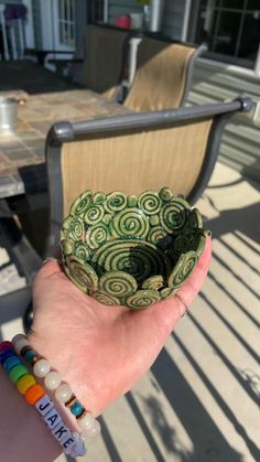 a hand holding a small green bowl with spiral designs on it