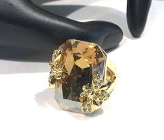 This gorgeous vintage  sparkly statement ring features a large rectangular shaped champagne coloured  faceted crystal with raised  pave  rhinestone flying insects on each side of the stone.  The sides of the ring has a triangle shape open work and  is a size 6.50 and the face 1" x .75" and is in very good/excellent condition with the champagne crystal excellent looking  very good/excellent and the gold tone great.  Unsigned and weighs 22 grams Shipping prices vary on the weight of item. I do my Gold Crystal Ring With Rectangular Stone For Wedding, Gold Crystal Ring With Bling For Party, Gold Crystal Ring For Party, Gold Crystal Ring With Diamond Accents For Party, Glamorous Gold Crystal Ring For Party, Gold Bling Crystal Ring For Party, Elegant Gold Rectangular Crystal Ring, Gold Crystal Ring With Rhinestones For Formal Occasions, Gold Crystal Ring With Rhinestones For Party