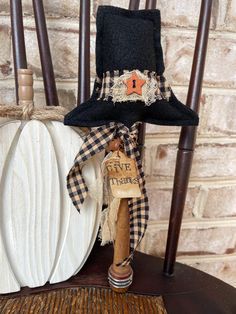 a black hat sitting on top of a wooden chair next to a white and orange pumpkin