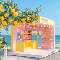 a lemonade stand on the beach with oranges hanging from it's roof