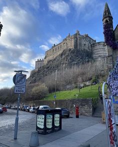 an old castle on top of a hill with purple flowers in the foreground and street signs