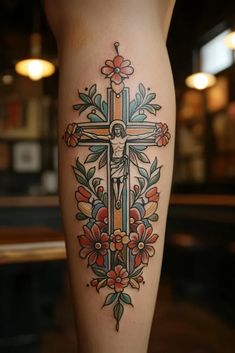 a cross with flowers and leaves on the side of a woman's leg in front of a bar