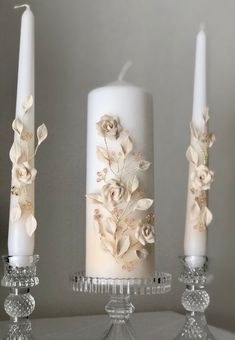 three white candles with flowers on them sitting next to each other