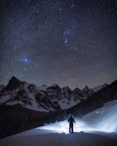 a man standing on top of a snow covered slope under a sky filled with stars