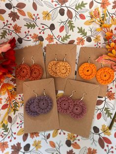 four pairs of crochet earrings are displayed on a table with autumn leaves in the background