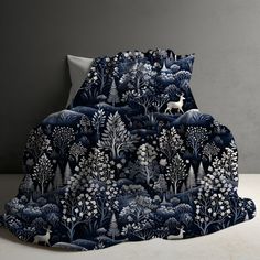 a bed covered in a blue and white blanket with trees, deers and flowers on it