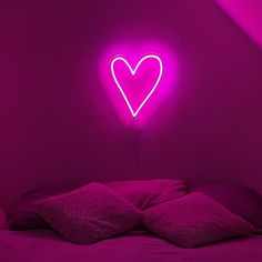 a heart shaped neon sign on the wall above a bed