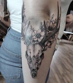 a woman with a deer skull and flowers on her arm