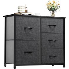 a black and gray cabinet with drawers on top of it, next to a vase filled with flowers