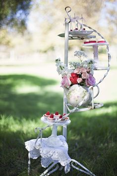 a tea party on a stand in the grass with flowers and cakes sitting on it