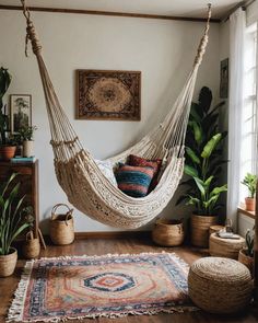 a hammock hanging from the ceiling in a room with potted plants and rugs