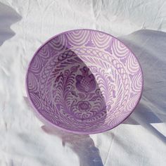 a purple bowl sitting on top of a white tablecloth covered floor next to a shadow