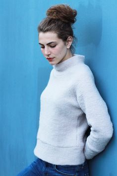 a woman leaning against a blue wall with her hands on her hips and looking down