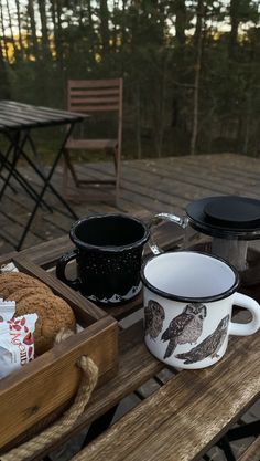 two coffee mugs sitting on top of a wooden table next to a box of cookies