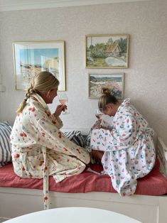 two women are sitting on a bed drinking wine and talking to each other while wrapped in blankets