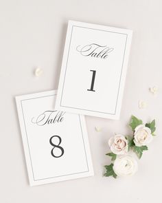 two place cards with white flowers and greenery on the side, one is for each table