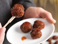 a person holding a plate with meatballs on it and a toothpick in their hand