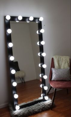 a large mirror with lights on it sitting in front of a chair next to a wall