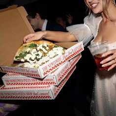 a woman in a white dress holding three pizzas with toppings on them and a glass of wine