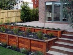 a wooden planter filled with lots of plants next to a brick wall and steps