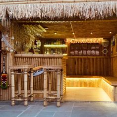 a bamboo bar with tiki style seating and lights on the outside, in front of it