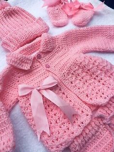 a pink knitted baby outfit and booties on a white blanket