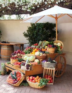 an outdoor market with lots of fruits and vegetables on display under an umbrella over the tables