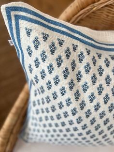 a blue and white pillow sitting on top of a wooden chair next to a wicker basket