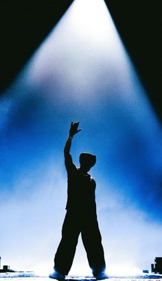 a person standing in front of a stage with their hand up to the sky and lights behind them