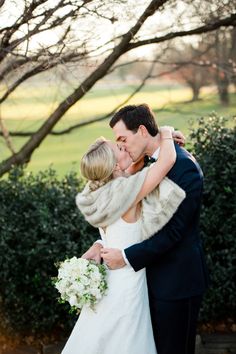 a bride and groom kissing in front of a tree with their arms around each other