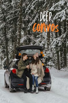 two people sitting in the back of a car on snow covered ground next to trees