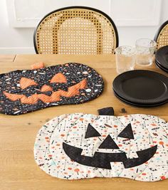 a wooden table topped with black plates and pumpkin placemats next to each other