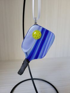 a blue and yellow glass object hanging from a black cord on a white table top