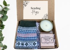 an open box containing socks, candle and soap on a white background with greenery