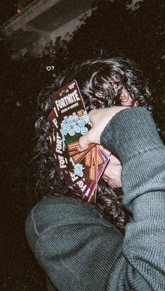 a person with long curly hair holding up a book in front of their face while sitting on the ground