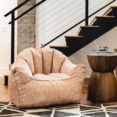 a chair and ottoman in front of a stair case next to a table with a book on it