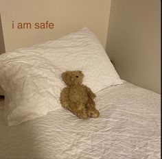 a brown teddy bear sitting on top of a white bed in a room with an i am safe sign above it