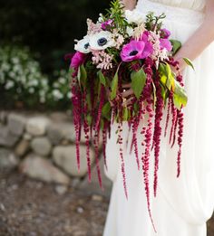 a woman holding a bouquet of flowers in her hands and wearing a white dress with purple accents