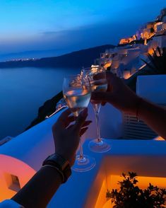 two people toasting with wine glasses on a balcony overlooking the ocean at night time