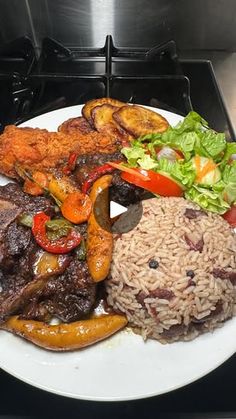 a white plate topped with meat, rice and veggies on top of a stove