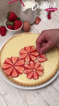 someone decorating a pie with strawberries on it