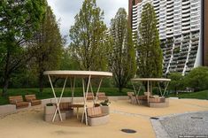 an empty park with benches and tables in the foreground, surrounded by tall buildings