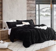 a bed with black and white comforters in a bedroom next to a window overlooking the snow covered mountains