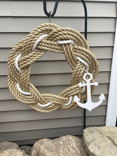 a rope wreath with an anchor hanging from the front of a house next to some rocks