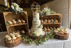 a wedding cake surrounded by cupcakes and greenery