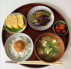 a wooden plate topped with bowls filled with different types of food next to chopsticks