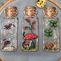 three glass bottles with flowers and bugs in them on a blue background cross stitched together