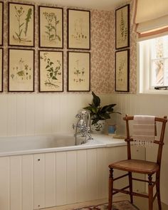 a chair sitting in front of a bath tub next to a wall with pictures on it