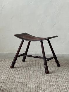 a wooden stool sitting on top of a carpeted floor next to a white wall